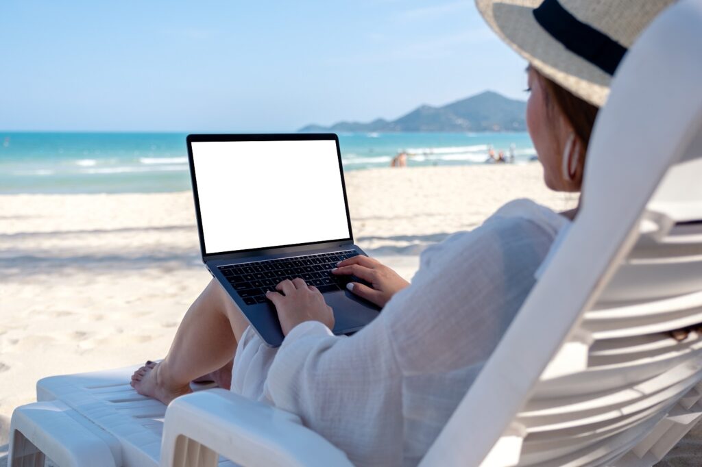 Woman using and typing on laptop computer while laying down on beach